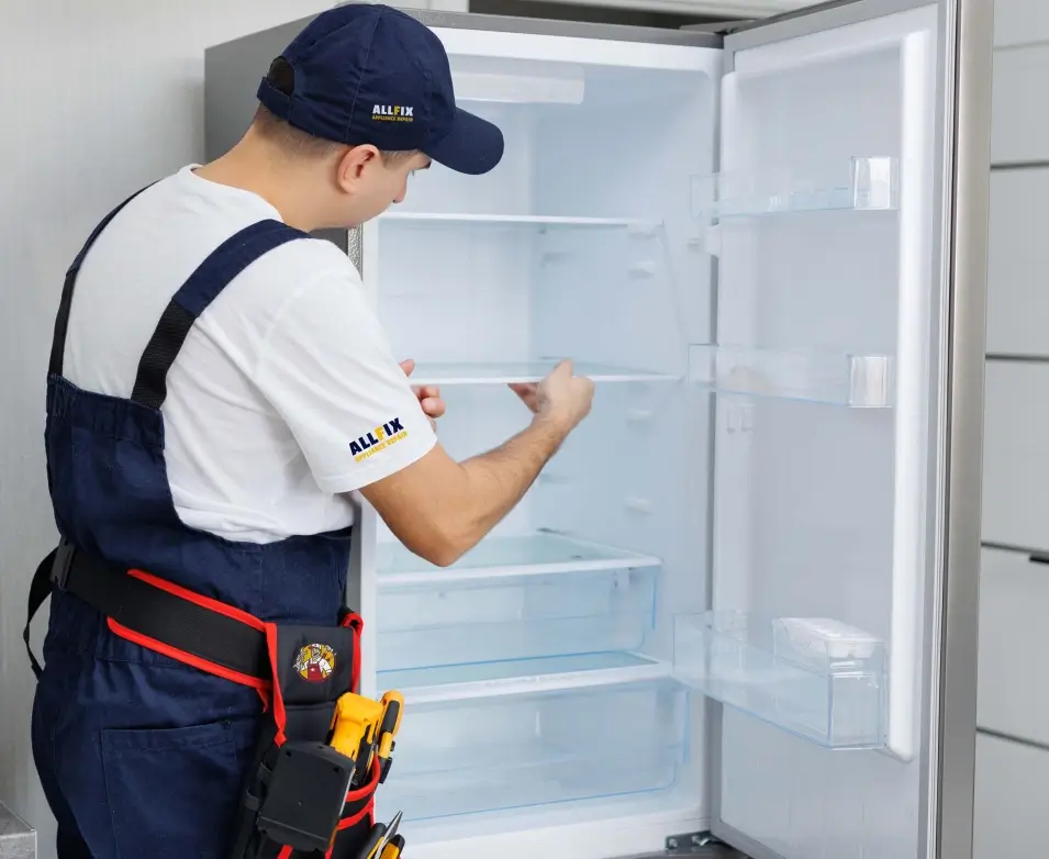 all fix appliance repair man in overalls and work boots stands before an open refrigerator