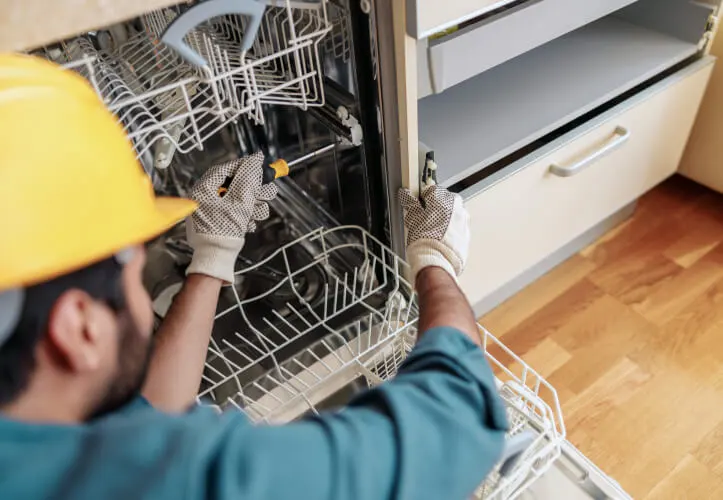 all fix appliance repair man wearing a hard hat and safety glasses repairs a dishwasher